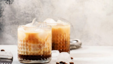 White russian cocktail, trendy alcoholic drink with vodka, coffee liqueur, cream and ice, gray background, bar tools