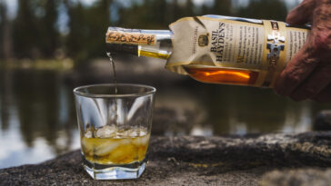 A closeup of a hand pouring Basil Hayden's bourbon whiskey in a glass