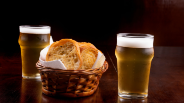 basket of toasted bread with garlic and two glasses of light beer on wooden table from the front