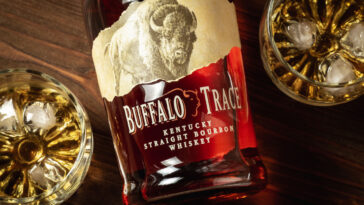 A bottle of Buffalo Trace Kentucky Straight Bourbon whiskey and two glasses with ice and bourbon on a wooden table