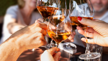 Family celebrating at dinner. Detail of hands while toasting with glasses of orange wine in a sunny day.
