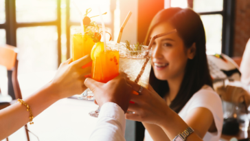 Beautiful and cheerful Asian woman cheering up for toast and celebration with friends in bar - focus on glasses