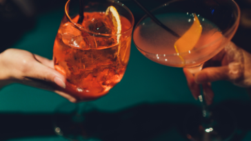 Hands of man and woman cheering with glasses of pink champagne.