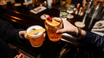 friends holding a glasses of alcoholic amaro nonino cocktails - sour mix and negroni with orange and cherry
