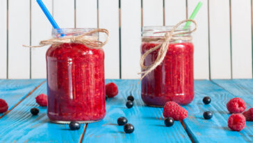 Glass mason jar with raspberry jam and fresh raspberries, blueberry