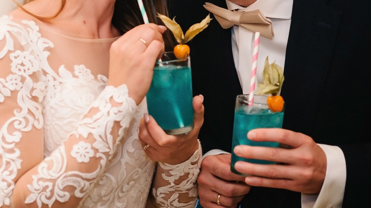 9 Most Popular Wedding Mocktails 1 The bride and groom holding a colorful cocktail in her hand. Man and woman hand hold fresh blue juice in the glass on the bar counter at night club in wedding day.