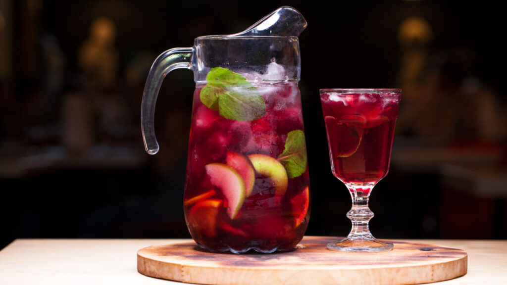 Homemade red wine sangria with orange, apple, strawberry and ice in glass and pitcher