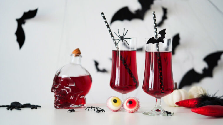 12 Best Vampire Cocktails to Try 1 Close-up of two bloody cocktails glass goblets for Halloween,bottle form skull,candy eyes,bats,spiders,pumpkins white background.