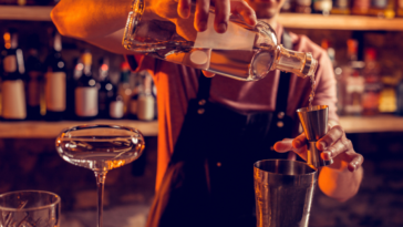Pouring vodka. Professional experienced barman wearing black apron pouring vodka for cocktail