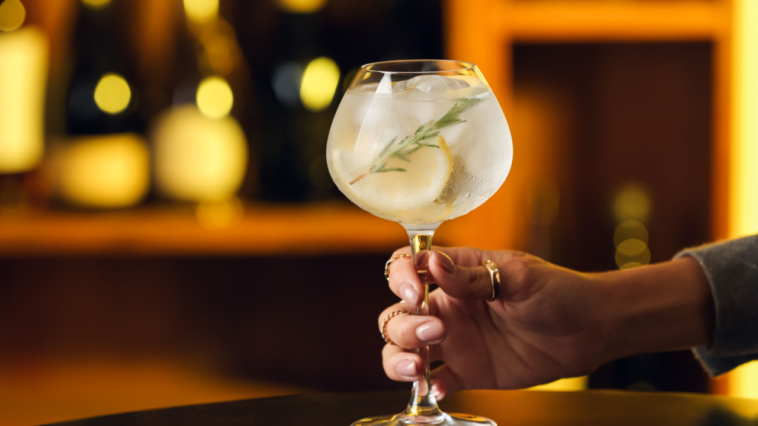 Female hand with glass of cold gin tonic on table in bar
