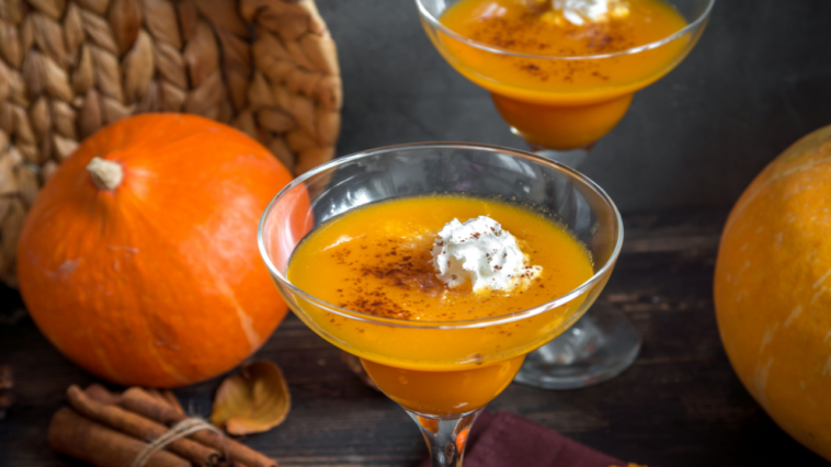 Fall Seasonal Drinks. Thanksgiving and Halloween Cocktails. Margarita Cocktail with Pumpkin Pie Spices and Whipped Cream on wooden table with autumn decor.