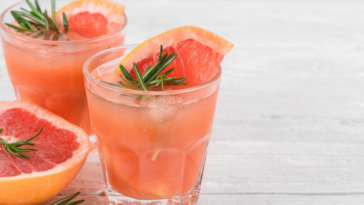 grapefruit cocktails in glasses with rosemary and ice on white background. Healthy citrus summer drink. close up