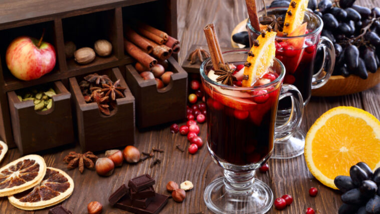Christmas mulled wine with apple, cranberry, orange, spices and chocolate on a wooden table