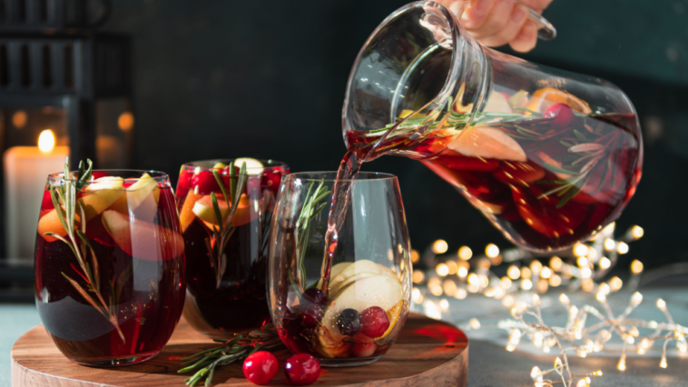 16 Best Christmas Sangria Recipes for This Season 1 red christmas sangria being poured from pitcher into wine glasses