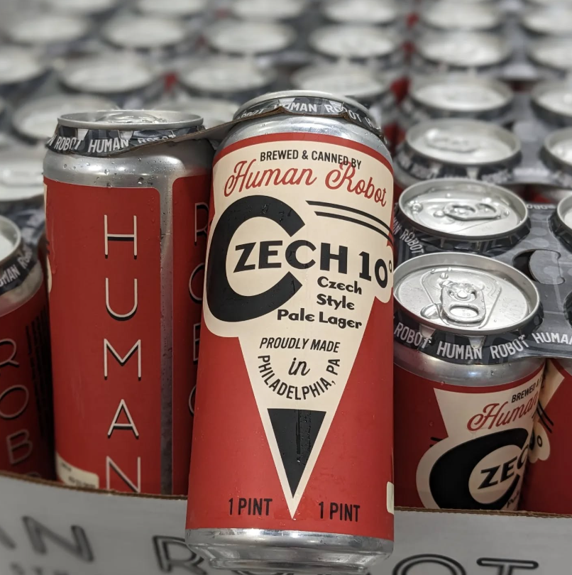 Cans of Human Robot Czech 10° Pale Lager proudly brewed in Philadelphia, PA are stacked together, showcasing bold red, cream, and black label design.