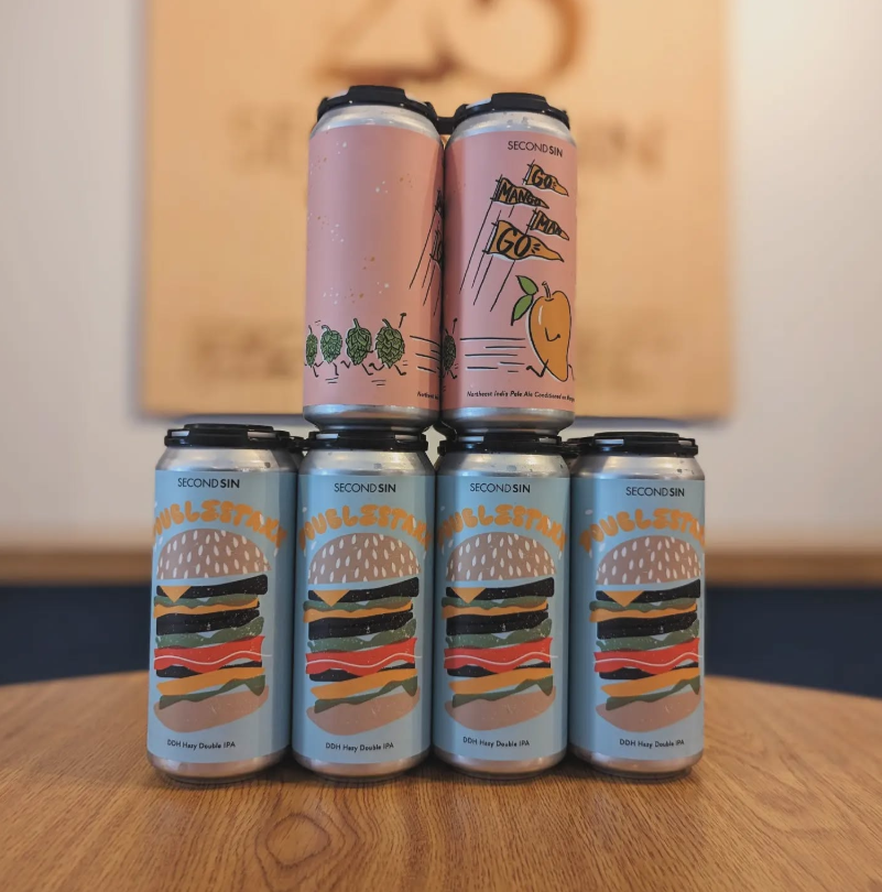 Six colorful cans from Second Sin Brewing feature two playful designs: a peach-themed pale ale and a DDH hazy double IPA with a stacked burger illustration.