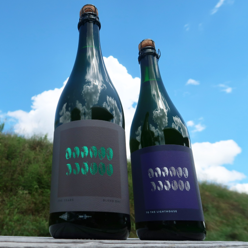 Two green glass bottles from The Referend Bier Blendery, one labeled “The Years Blend One” with a gray label and green foil text, set against a blue sky.