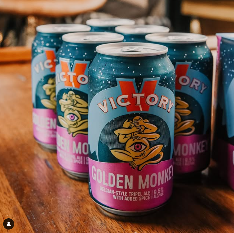 Cans of Victory Brewing Company's Golden Monkey Belgian-style tripel ale with bold artwork featuring a meditating monkey and pink, blue, and orange design.
