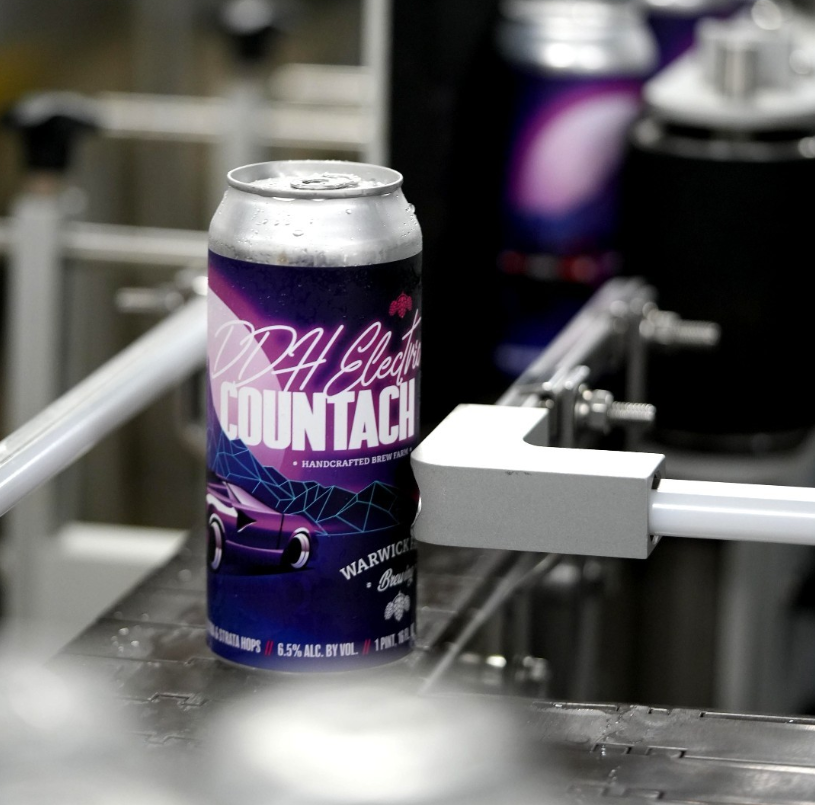 A can of Warwick Farm Brewing’s DDH Electric Countach, with a bold purple and pink retro design, is shown on a brewery conveyor system during production.